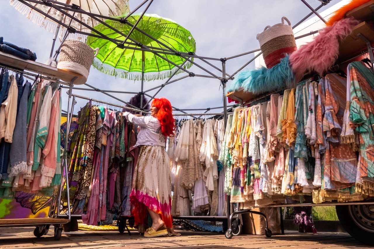 Kraampje Ibizafestival: kleurige kleding, dame met felrood haar, parasols