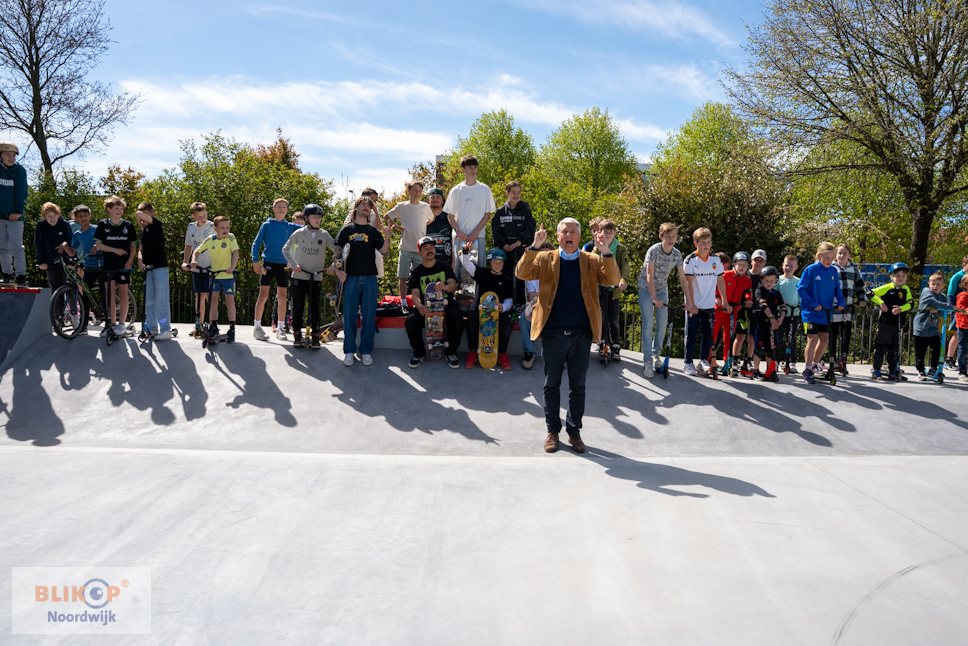 Een groep skaters staat op een skatebaan achter de wethouder die het park opent
